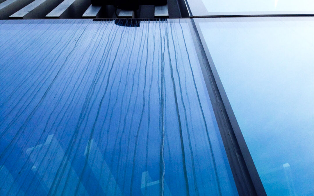 Glasfassade mit sichtbaren Verätzungs- und Glaskorrosionsspuren durch Zementschleier nach Bauarbeiten.